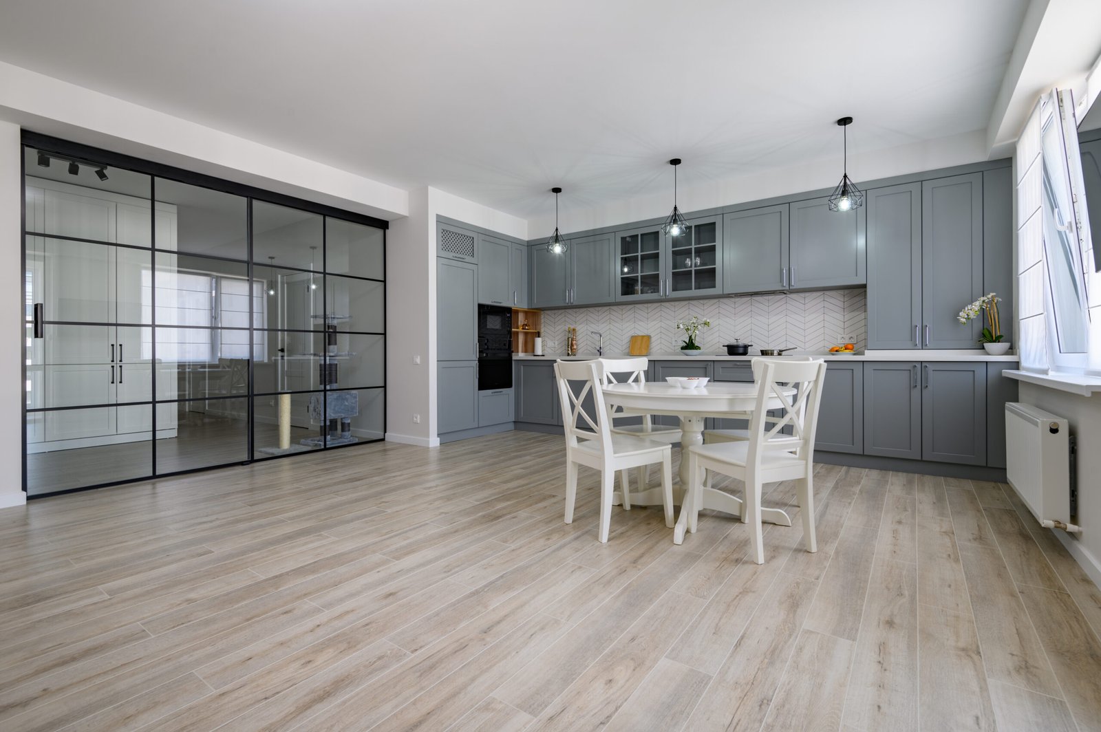 Trendy grey and white modern kitchen with white round dining table in studio apartment